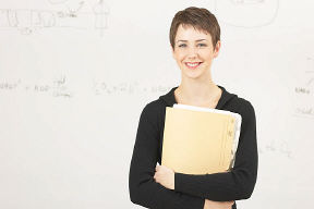 smiling teacher holding folder in front of a white board